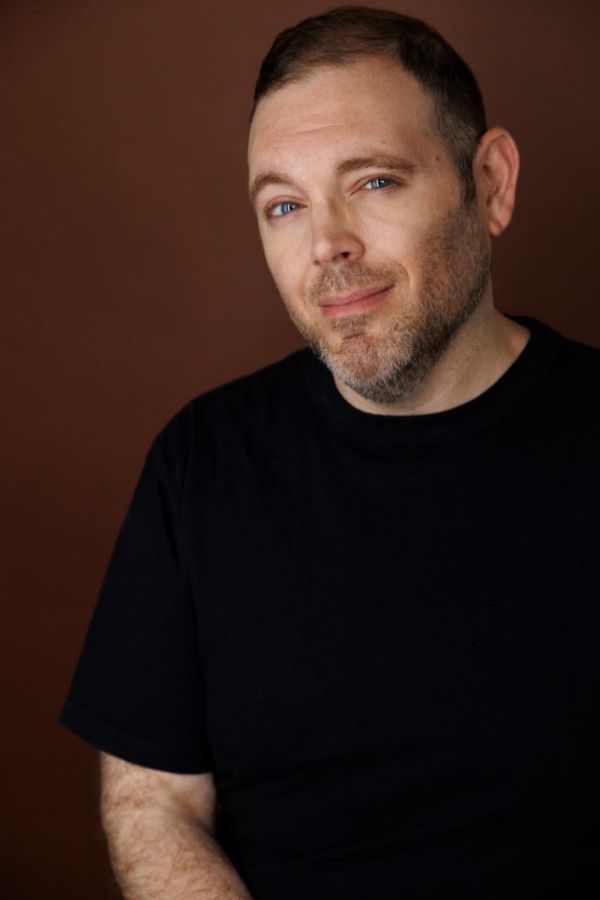 Justin Restivo in a black shirt against a warm brown background