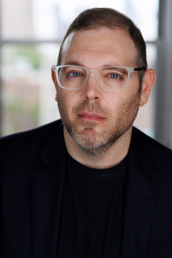 Justin Restivo wearing clear glasses and a dark blazer